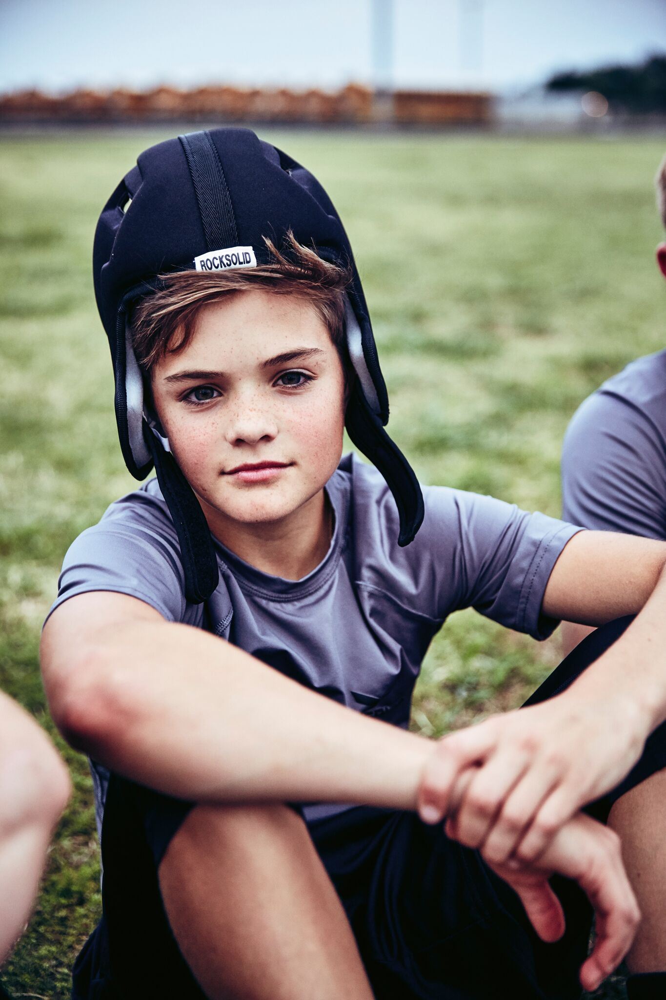Young athlete in Rocksolid soft shell headgear sitting beside the field